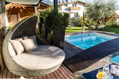 a wicker chair sitting on a deck next to a swimming pool at Hotel Alpenhof in Tirolo