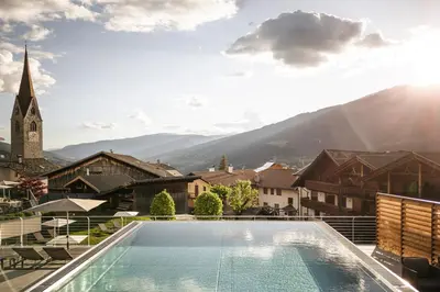 a swimming pool in front of a building with a church at Hotel Gasserhof in Bressanone
