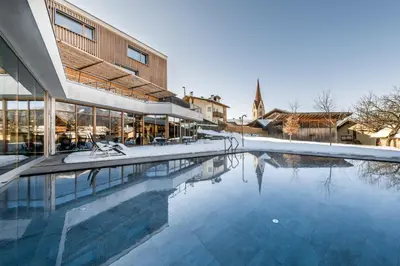 a swimming pool in front of a building with a church at Hotel Gasserhof in Bressanone