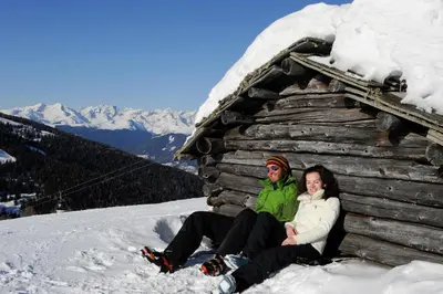 a man and woman sitting in the snow next to a cabin at Apartment Obermair in Brunico