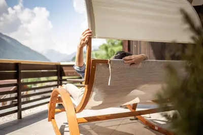 a woman sitting in a rocking chair on a balcony at Pöder - daheim in den Bergen in Ultimo
