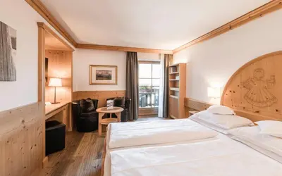 a bedroom with a bed and a desk and a window at Hotel Angelo Engel in Ortisei
