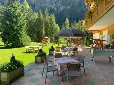a patio with tables and chairs and an umbrella at Alpenhotel Panorama in Campitello di Fassa