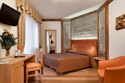 a bedroom with a bed and a desk and a television at Alpenhotel Panorama in Campitello di Fassa