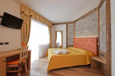 a bedroom with a bed and a desk and a television at Alpenhotel Panorama in Campitello di Fassa
