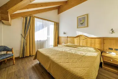 a bedroom with a bed and a large window at Alpenhotel Panorama in Campitello di Fassa