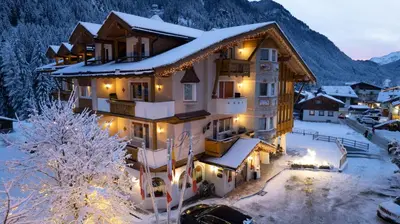 a house in the snow with lights on at Alpenhotel Panorama in Campitello di Fassa