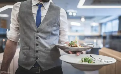 a man holding two plates of food in a restaurant at Molaris Lodge in Mühlbach