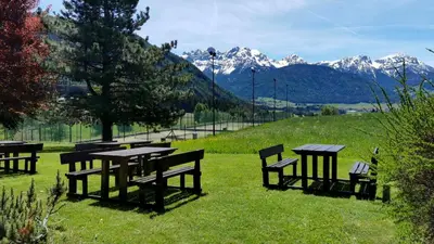 a group of picnic tables and benches in a field with mountains at Smy Koflerhof Wellness & Spa Dolomiti in Rasun di Sopra
