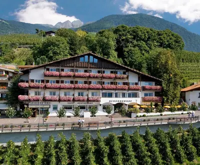 a hotel with a river in front of a mountain at Hotel Schennerhof in Schenna