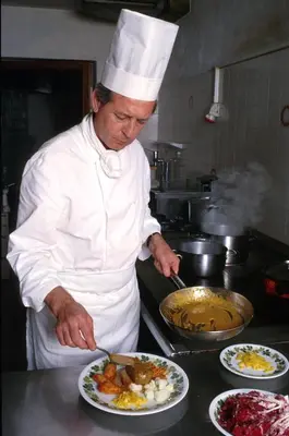a chef preparing food in a kitchen with plates of food at Hotel Rainegg in Valdaora