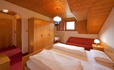 a bedroom with two beds and a red couch at Hotel Rainegg in Valdaora
