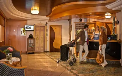 a man and woman with luggage in a hotel lobby at Aktiv & Relax Hotel Hubertus in Villandro