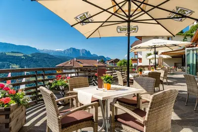 a patio with tables and chairs and an umbrella at Aktiv & Relax Hotel Hubertus in Villandro