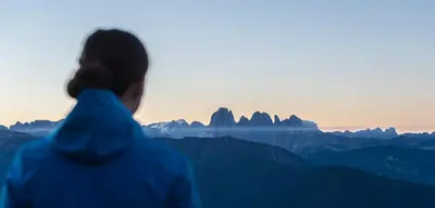 a person standing on top of a mountain looking at the mountains at Aktiv & Relax Hotel Hubertus in Villandro