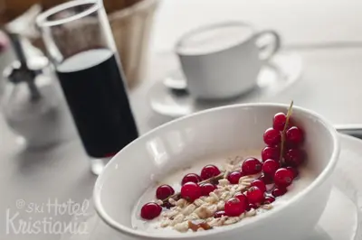 a bowl of oatmeal with cranberries and a glass of soda at Kristiania Small Dolomites Hotel in Selva di Val Gardena