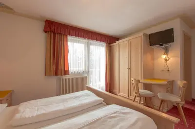 a bedroom with a bed and a desk and a window at B&B Apartments La Palsa in San Cassiano