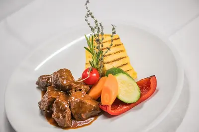 a white plate of food with meat and vegetables at Gasthof Albergo Dolomiten in Braies