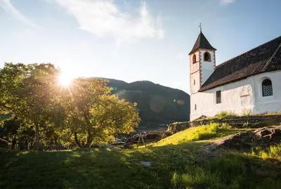 an old church on a hill with the sun shining at Mondschein Rooms in Lana