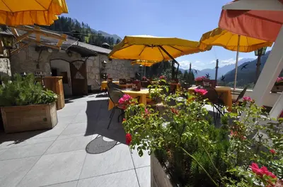 a patio with tables and yellow umbrellas and flowers at Hotel Al Forte in Arabba