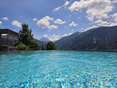 a pool of blue water with mountains in the background at Hotel Kompatscherhof in Luson