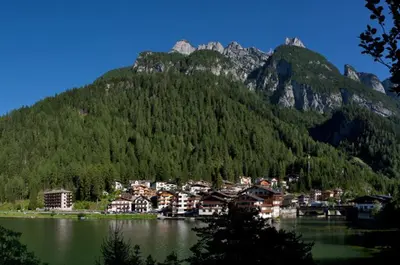 a town in front of a mountain with a body of water at Appartamenti Regina in Alleghe