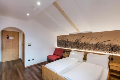 a bedroom with a bed and a red chair at Berghotel Schlemmer in Bressanone