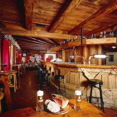 a bar in a restaurant with wooden ceilings and bar stools at Hotel Garni San Nicolò in Pozza di Fassa
