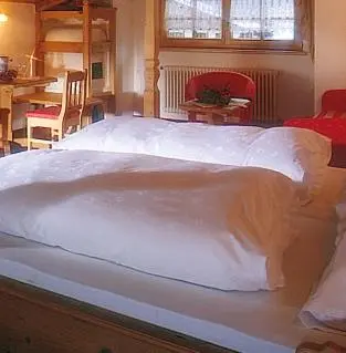 a large white bed in a room with a table at Hotel Garni San Nicolò in Pozza di Fassa