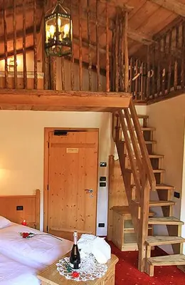 a room with a bed and a staircase with a bottle of wine at Hotel Garni San Nicolò in Pozza di Fassa