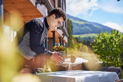 a man standing at a table with a vase of flowers at Naturhotel Die Waldruhe GmbH in Chienes