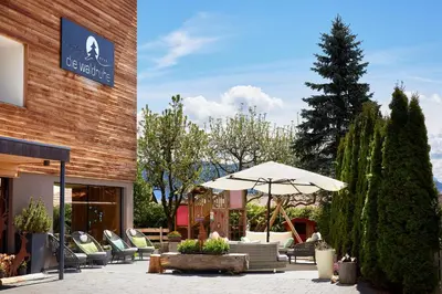 a patio with chairs and an umbrella in front of a building at Naturhotel Die Waldruhe GmbH in Chienes