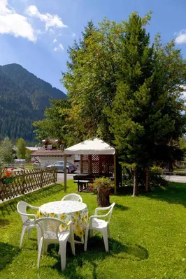 a table and chairs with an umbrella in the grass at Garni Tyrolia in Campitello di Fassa