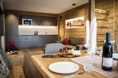 a kitchen and living room with a table with a bottle of wine at Apartments Grunnes in Ortisei