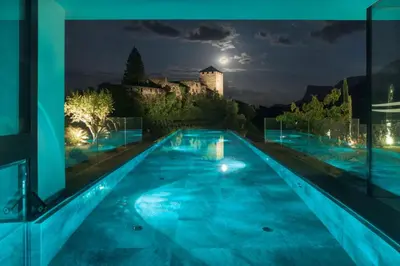 a swimming pool at night with a castle in the background at Hotel Der Waldhof in Vollan