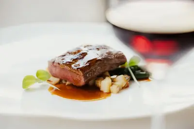 a piece of meat on a plate with a glass of wine at Hotel Genziana in Ortisei