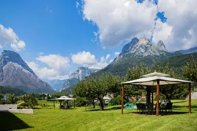 a picnic table with an umbrella in a field with mountains at Hotel Villa Imperina in Agordo