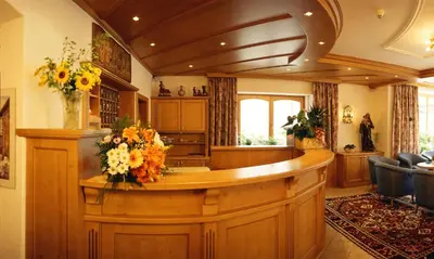 a lobby with a counter with flowers on it at Hotel Dolomiti Madonna in Ortisei