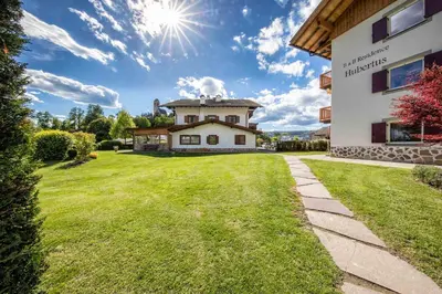 a house with a green lawn in front of a building at hubertus dolomites in Fiè