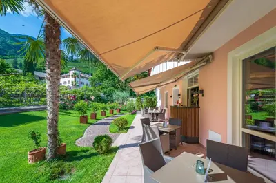 an outdoor patio with tables and chairs and palm trees at Gartenheim Tramin in Termeno