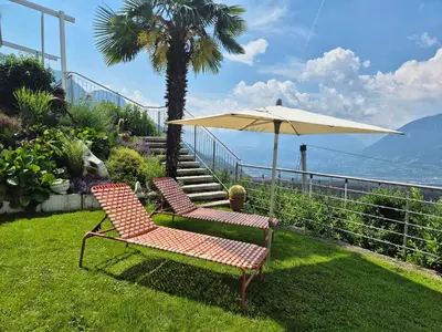 two chairs and an umbrella sitting on the grass at Apartments Graf Hartwig in Schenna
