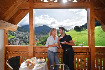 a man and woman standing on a porch with a table at Alpin & Vital Hotel La Perla in Ortisei