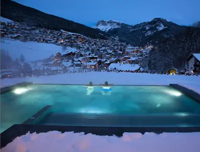 a swimming pool in the snow with a town in the background at Alpin & Vital Hotel La Perla in Ortisei