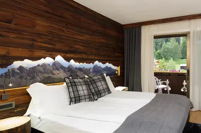 a bedroom with a white bed with a wooden wall at Sport Hotel Majarè in Pozza di Fassa