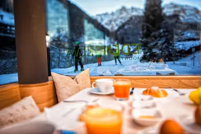 a table with food and drinks and a view of a ski resort at Mountain Design Hotel Eden Selva in Selva di Val Gardena