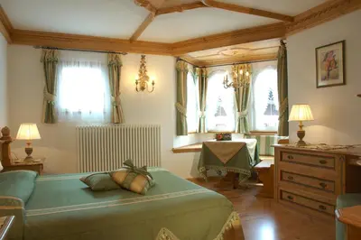 a bedroom with a bed and a table and windows at Hotel Letizia in San Martino di Castrozza
