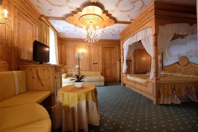 a bedroom with a canopy bed with a table and a chandelier at Hotel Letizia in San Martino di Castrozza