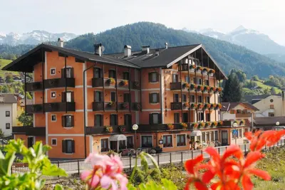 a large building on a hill with mountains in the background at Albergo Conca Verde in Fiera di Primiero