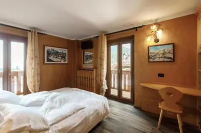 a bedroom with a bed and a desk and windows at B&B La Montanara in San Martino di Castrozza