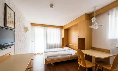 a room with a bed and a desk and a television at Residence Antares in Selva di Val Gardena